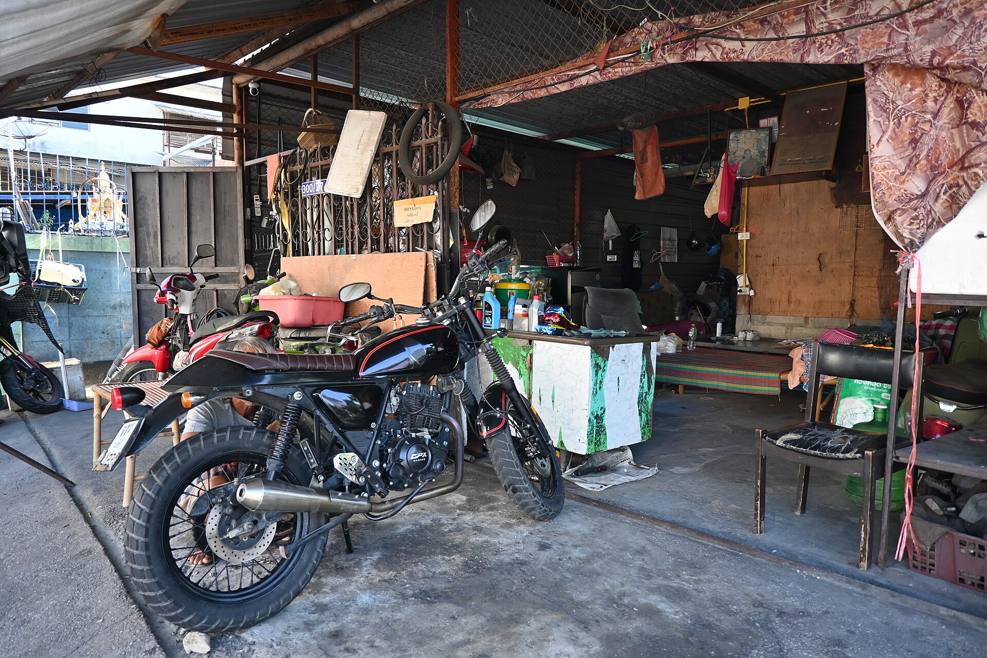 DFC 3998 A rugged motorcycle parked in front of a small well used workshop filled with tools and spare parts