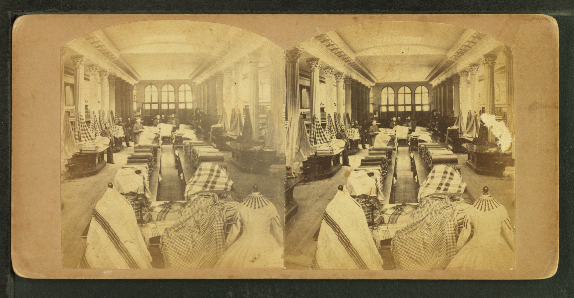 Interior view of C.F. Hovey and Co., showing salesmen among counters piled with fabric and a dress on form in the foreground, by C.H. Wheeler & Co.