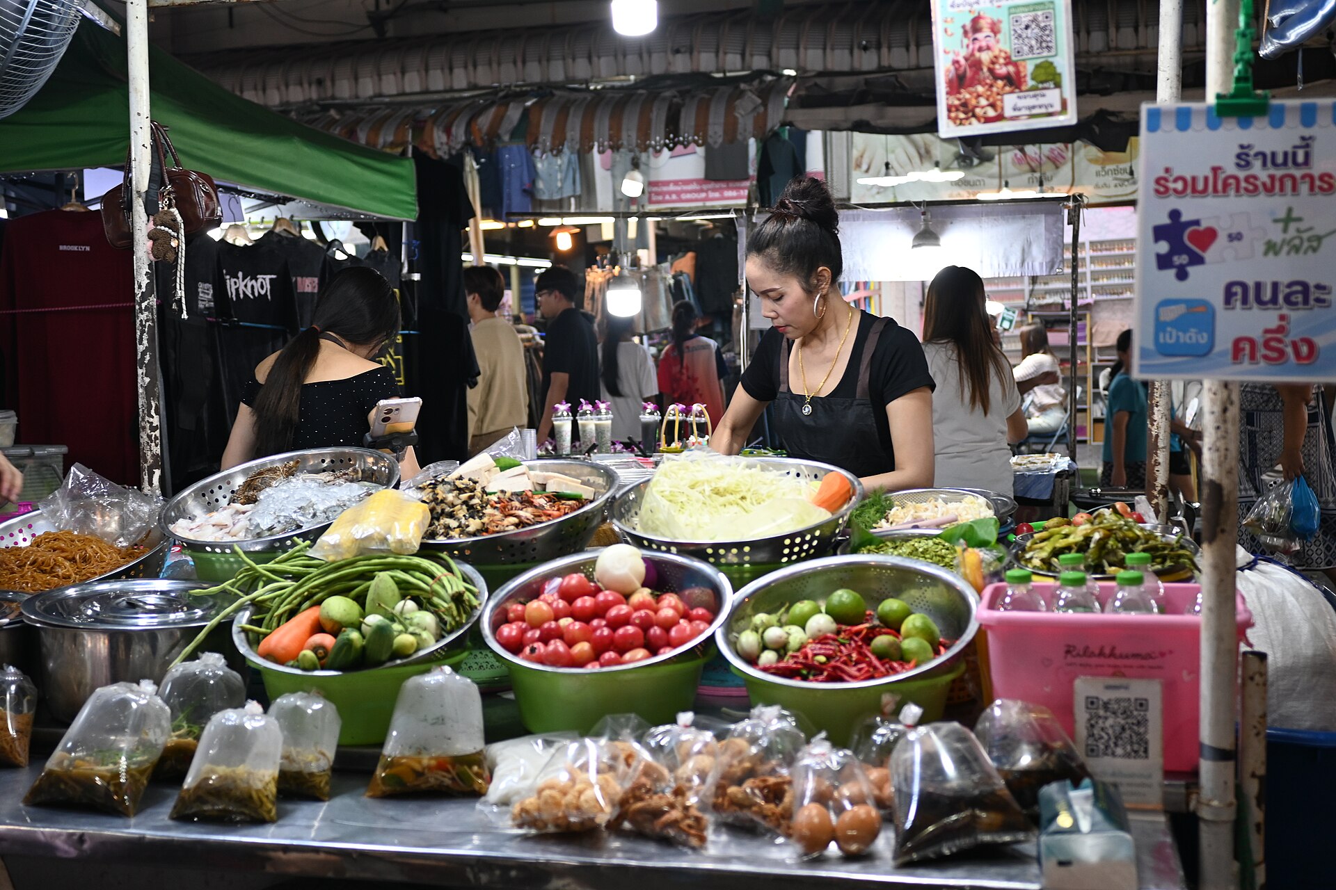 DFC 3508 A bustling night market food stall displaying bowls of fresh vegetables herbs and colorful produce while a vendor prepares dishes behind the counter
