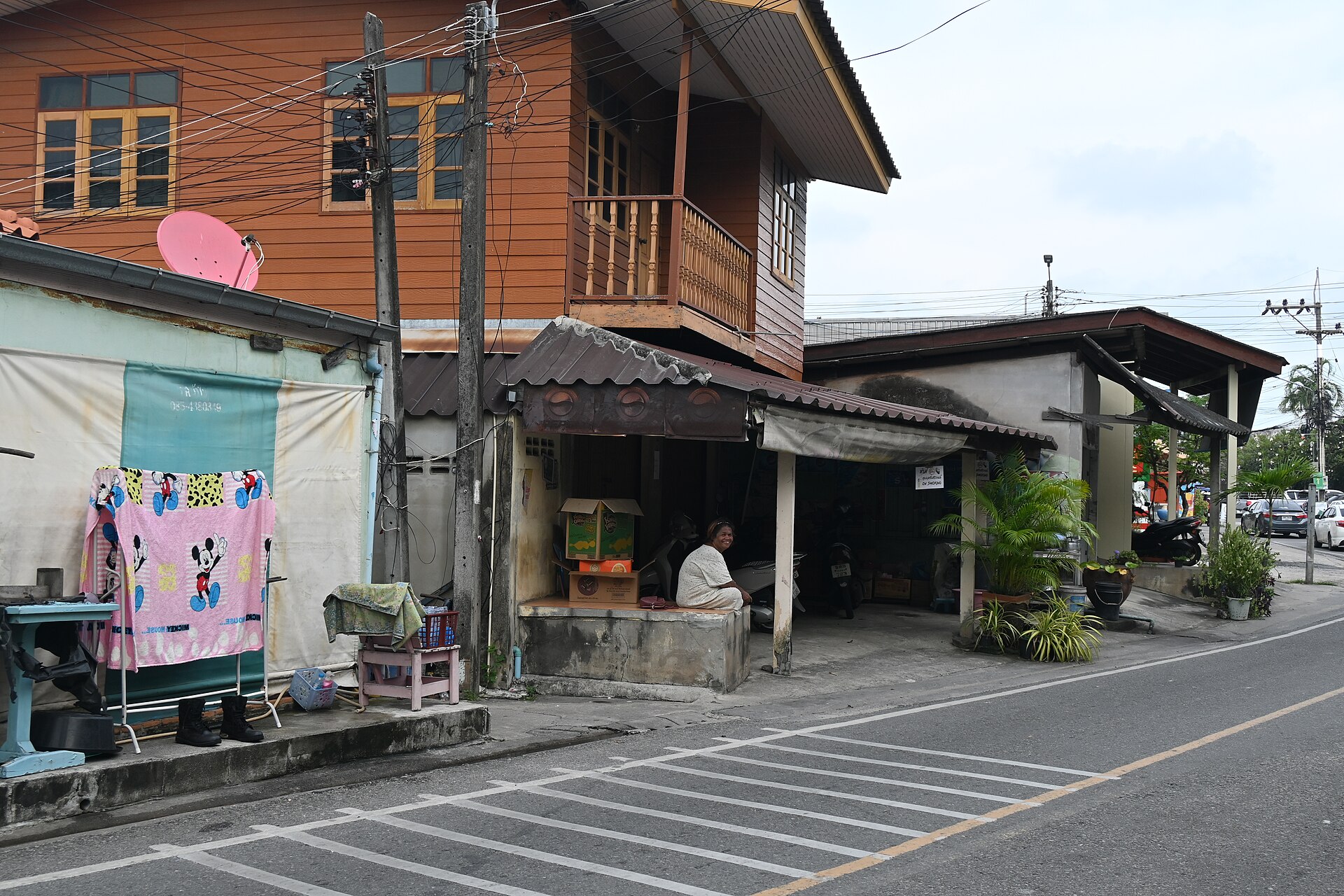 DFC 2174 A quiet street scene with a wooden house and small storefronts a person sitting under an awning and laundry hanging out to dry