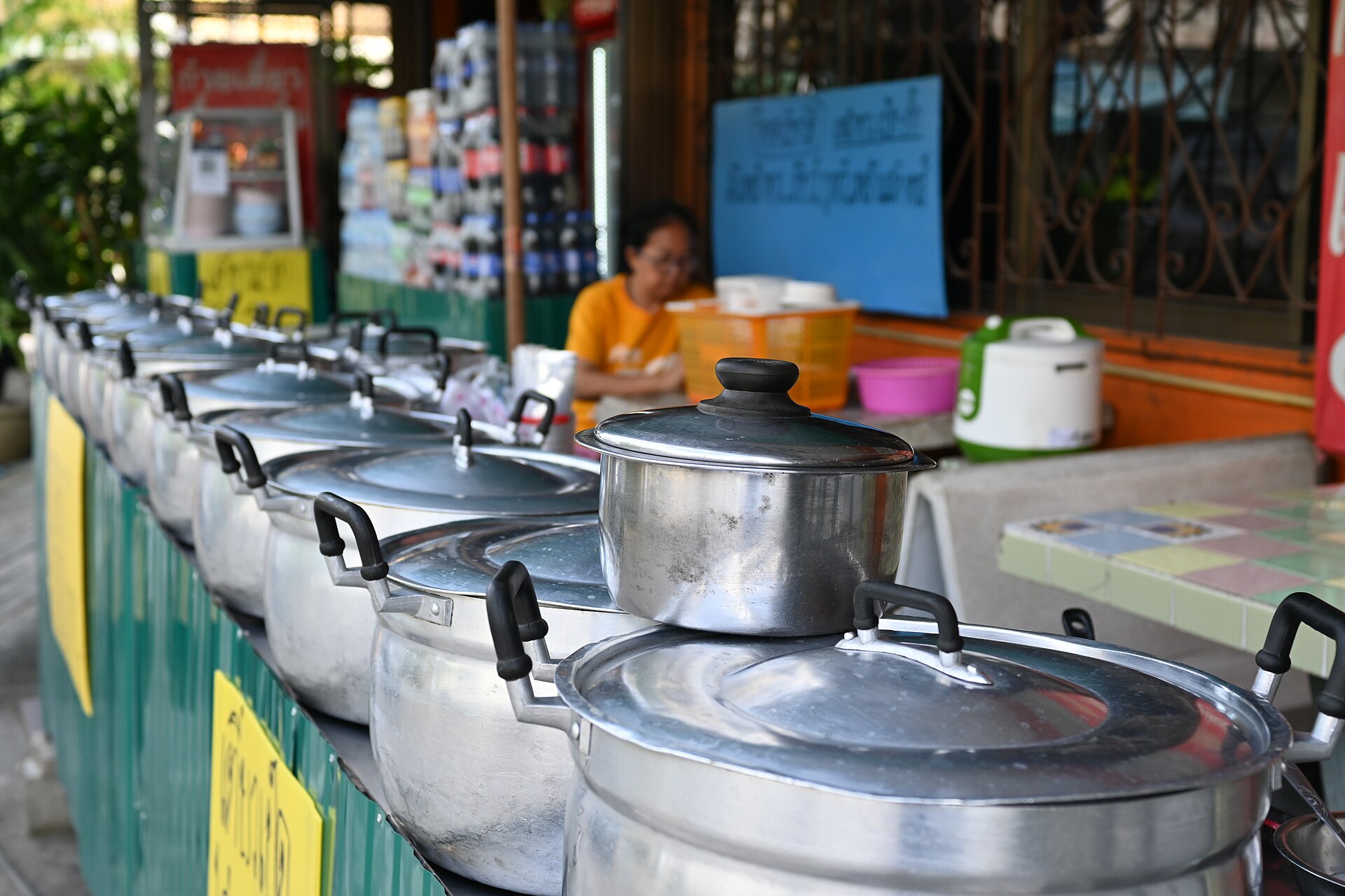 DFC 0168 A row of steaming metal pots lined up at a street food stall with the vendor seated in the background