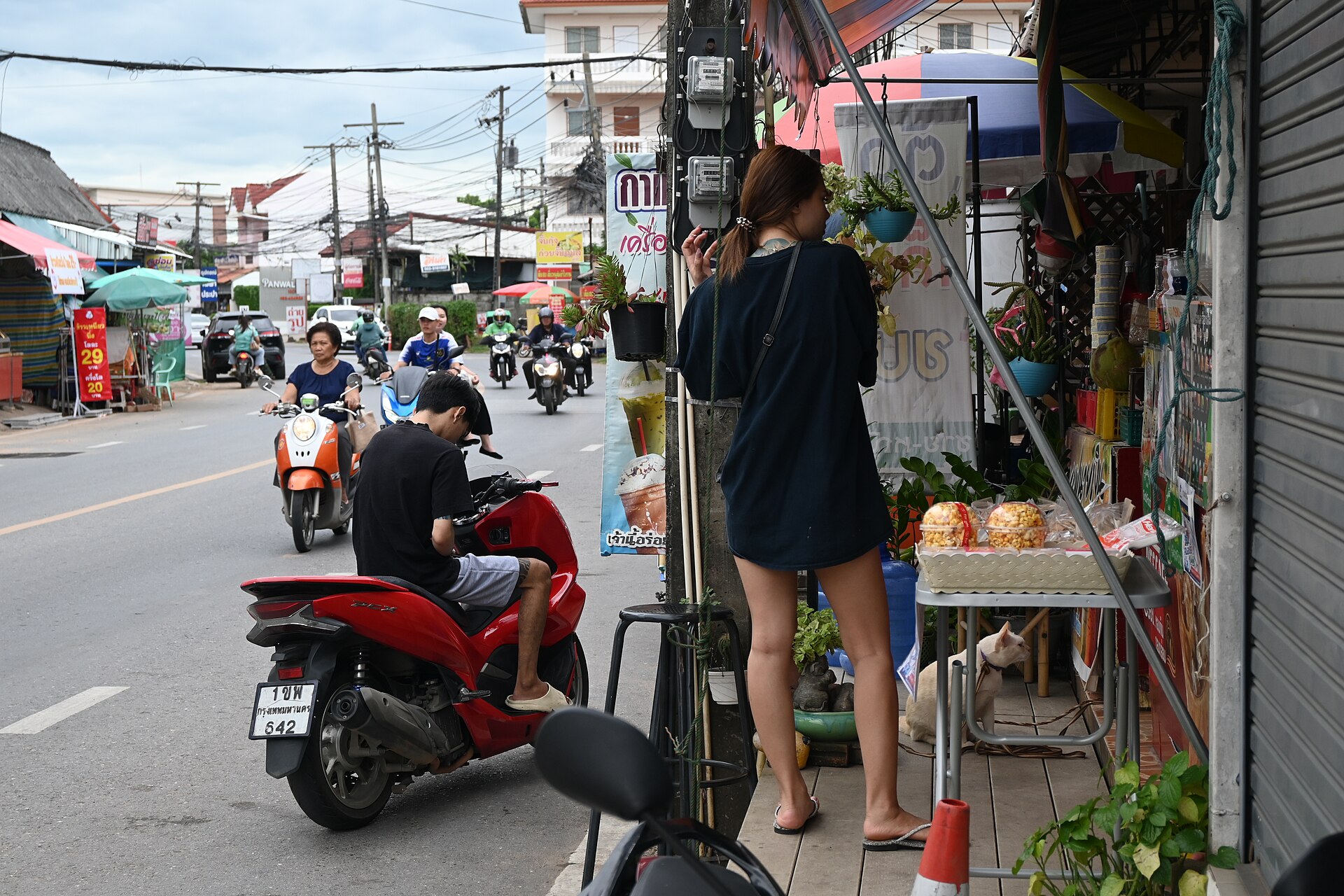 DFC 2422 A street vendor arranges goods at a small sidewalk stall while scooters and motorcycles pass by on a busy urban road